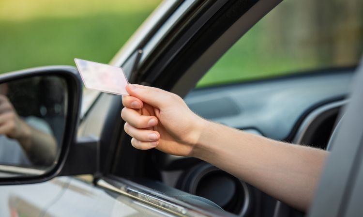 Man handing his drivers license out of the driver window of his car