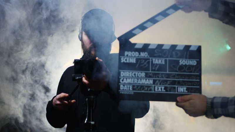 Film maker holding a camera while in a smokey alley